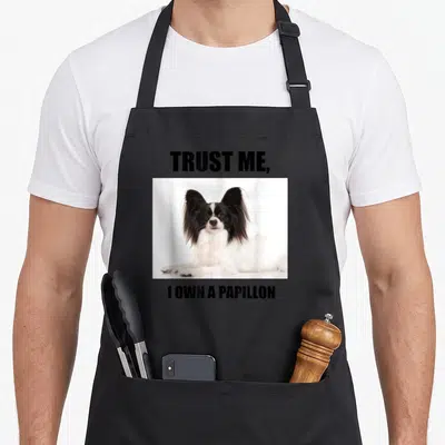 Vintage papillon apron - Photo of black and white Papillon dog between bold text reading Trust Me I Own a Papillon — shown on a black cotton canvas apron against a white background