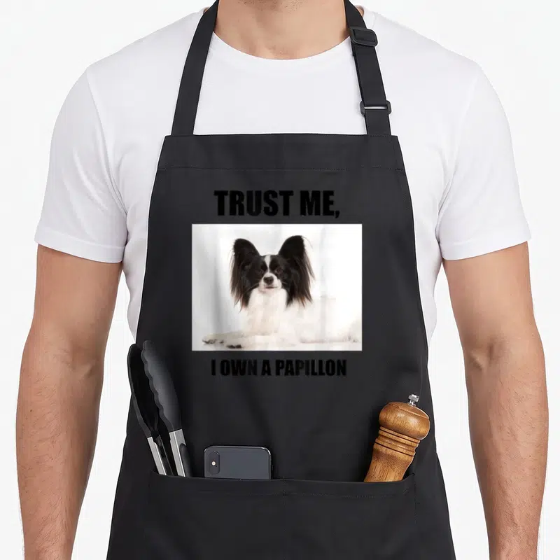 Vintage papillon apron - Photo of black and white Papillon dog between bold text reading Trust Me I Own a Papillon — shown on a black cotton canvas apron against a white background