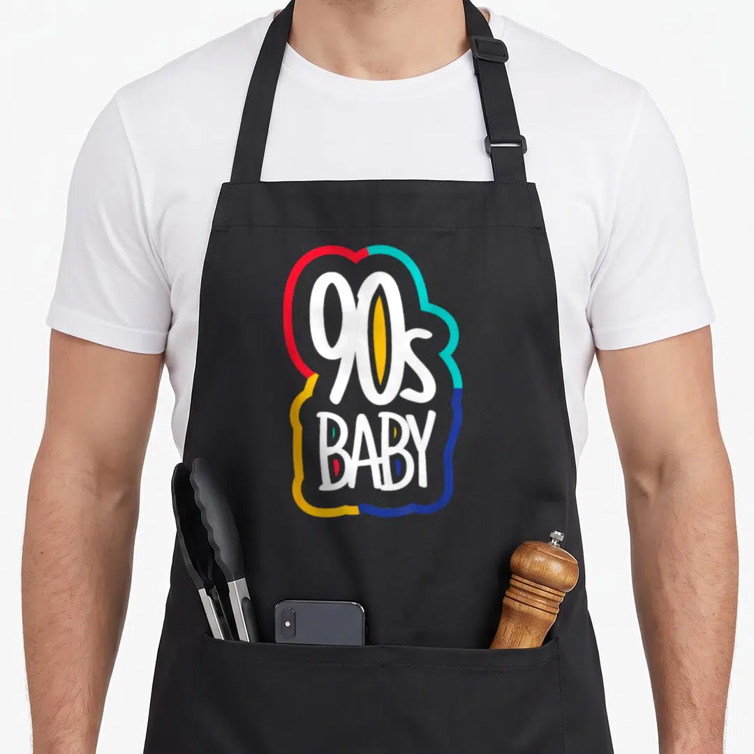 Baby 90s apron - White 90s BABY text inside red cyan yellow blue grey abstract outline — shown on a black cotton canvas apron against a white background