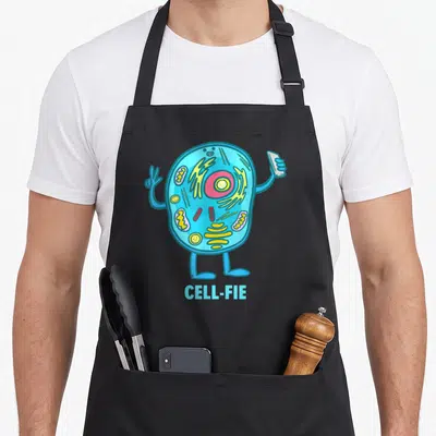 Fie teacher apron - Cartoon cell character holding phone and peace sign with text CELL-FIE below — shown on a black cotton canvas apron against a white background