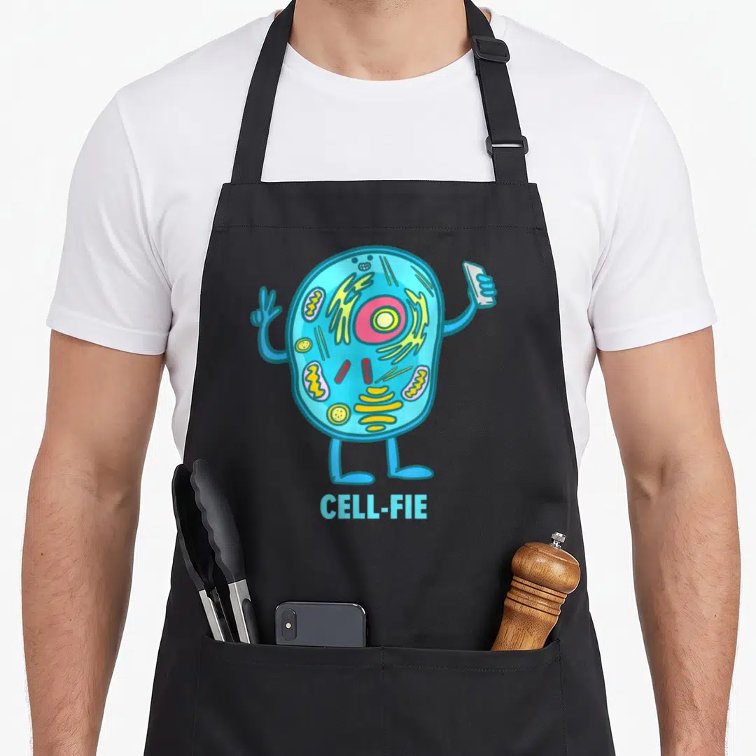 Fie teacher apron - Cartoon cell character holding phone and peace sign with text CELL-FIE below — shown on a black cotton canvas apron against a white background
