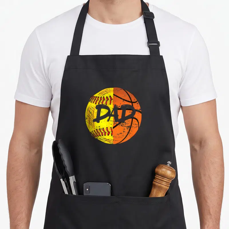 Basketball sports dad apron - Split yellow softball and orange basketball with grey DAD text in distressed style — shown on a black cotton canvas apron against a white background
