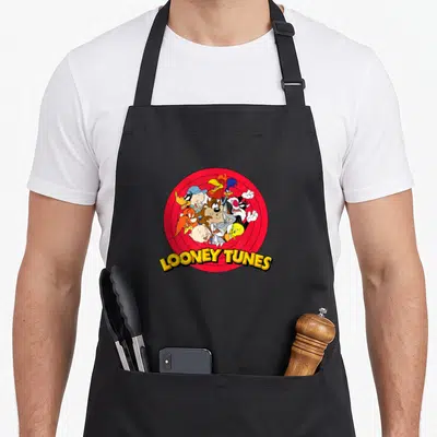 Funny yosemite apron - Looney Tunes characters clustered in red target with yellow curved text — shown on a black cotton canvas apron against a white background