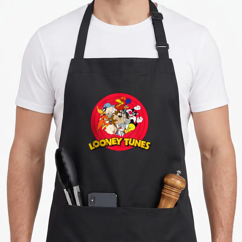Funny yosemite apron - Looney Tunes characters clustered in red target with yellow curved text — shown on a black cotton canvas apron against a white background