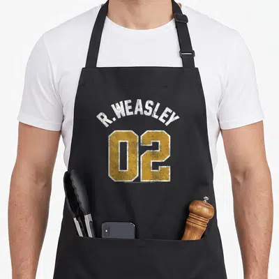 Weasley novelty apron - R. WEASLEY 02 yellow and white distressed jersey text on black background — shown on a black cotton canvas apron against a white background