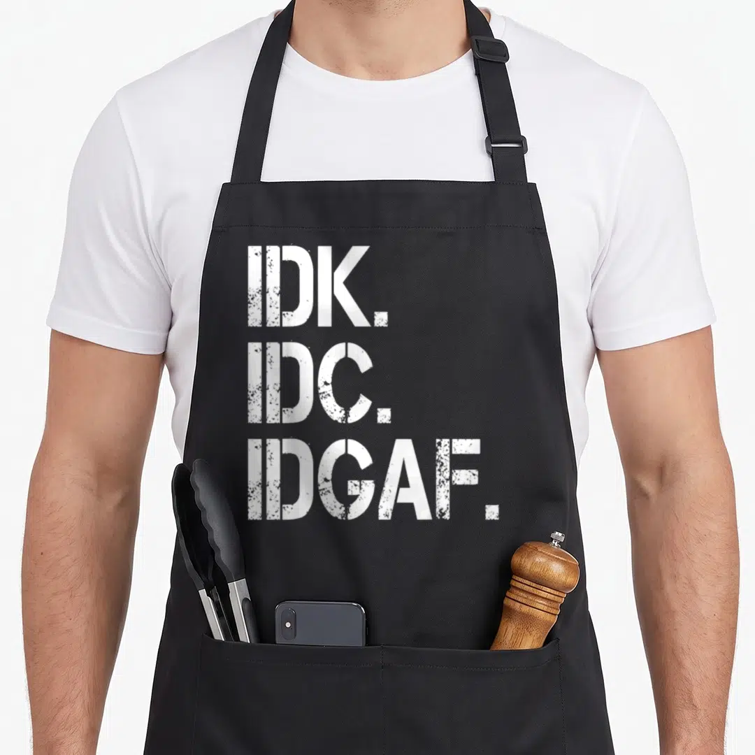 Idk idc idgaf apron - Three lines of white distressed text reading IDK IDC IDGAF — shown on a black cotton canvas apron against a white background