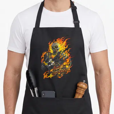 Ghost skull apron - Flaming grey skeleton with orange flames and SPIRIT OF VENGEANCE ribbon text — shown on a black cotton canvas apron against a white background