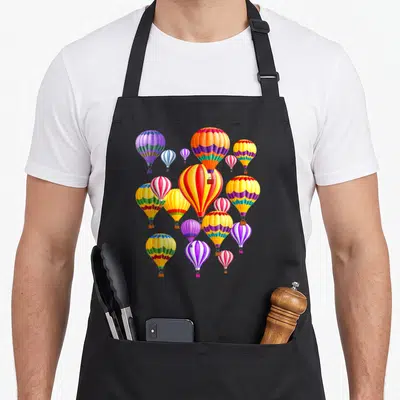 Colorful hot balloon apron - Cluster of cartoon hot air balloons in red, yellow, blue, purple, and green stripes — shown on a black cotton canvas apron against a white background