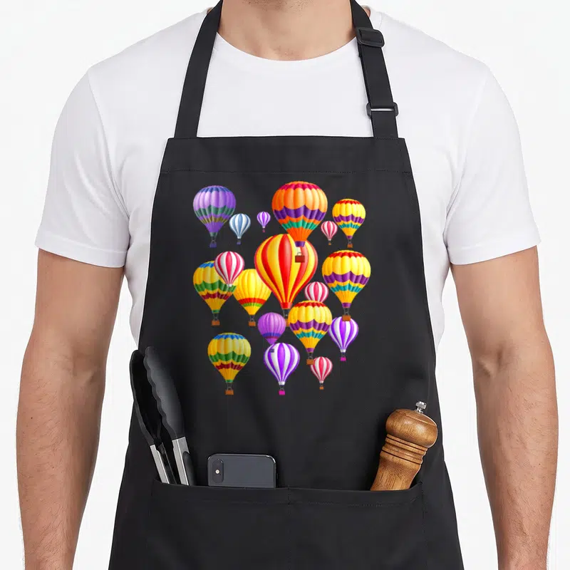 Colorful hot balloon apron - Cluster of cartoon hot air balloons in red, yellow, blue, purple, and green stripes — shown on a black cotton canvas apron against a white background