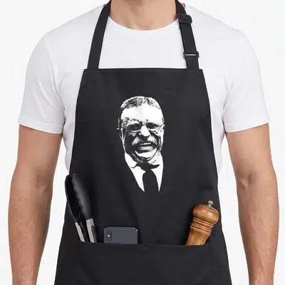 Smiling teddy apron - White silhouette portrait of laughing man with glasses and tie — shown on a black cotton canvas apron against a white background