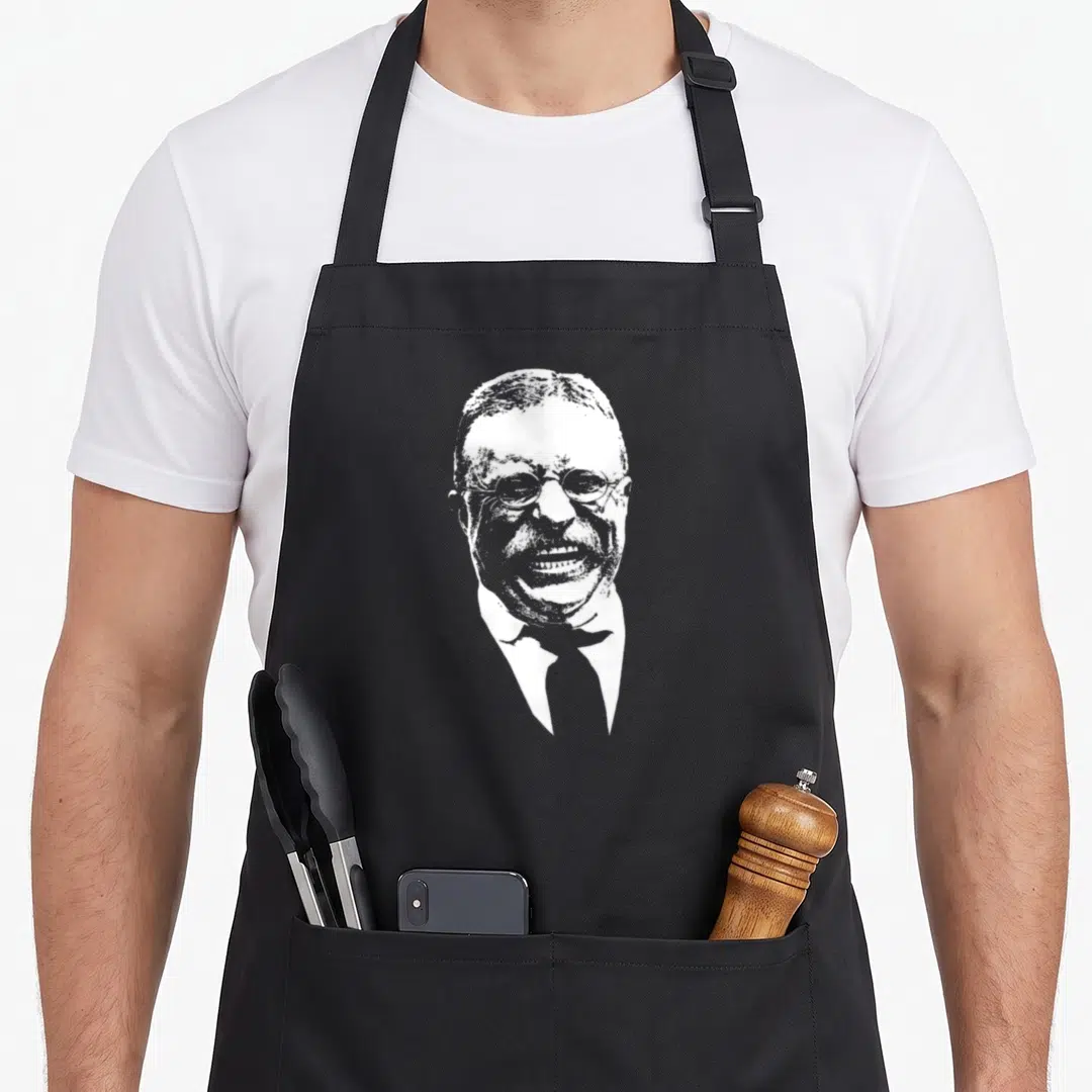 Smiling teddy apron - White silhouette portrait of laughing man with glasses and tie — shown on a black cotton canvas apron against a white background