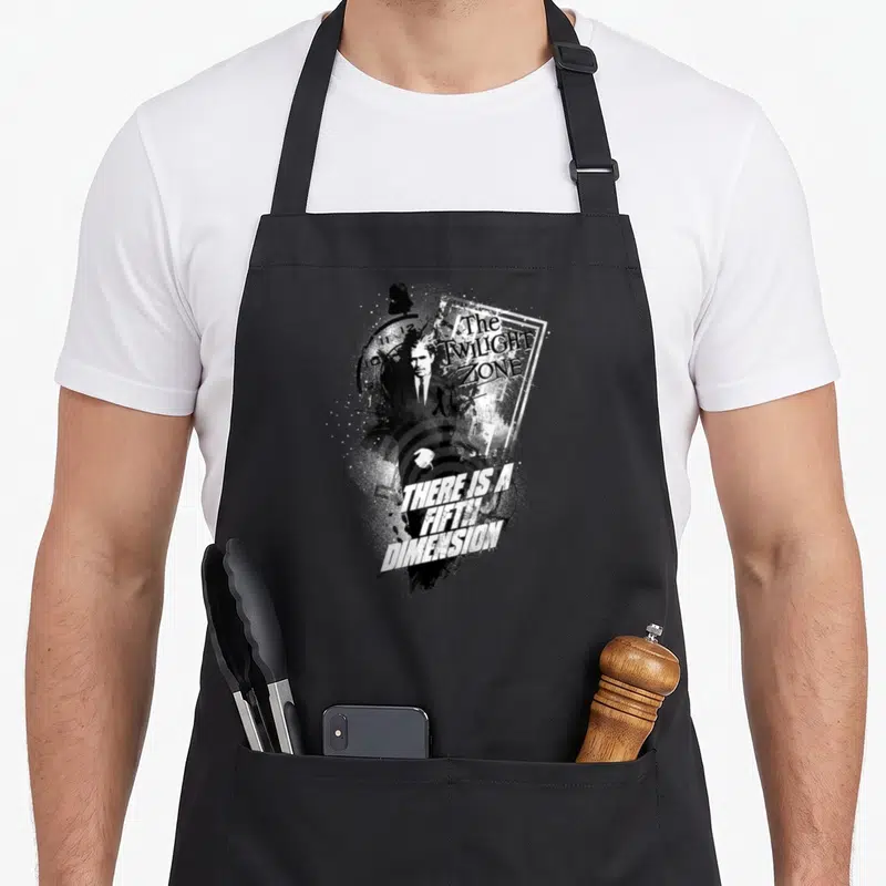 Fifth twilight apron - Man's face and clock face with There Is A Fifth Dimension text in distressed black and white — shown on a black cotton canvas apron against a white background