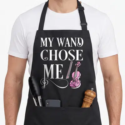 Wand violinist apron - White stacked text reading My Wand Chose Me beside pink violin and treble clef flourish — shown on a black cotton canvas apron against a white background