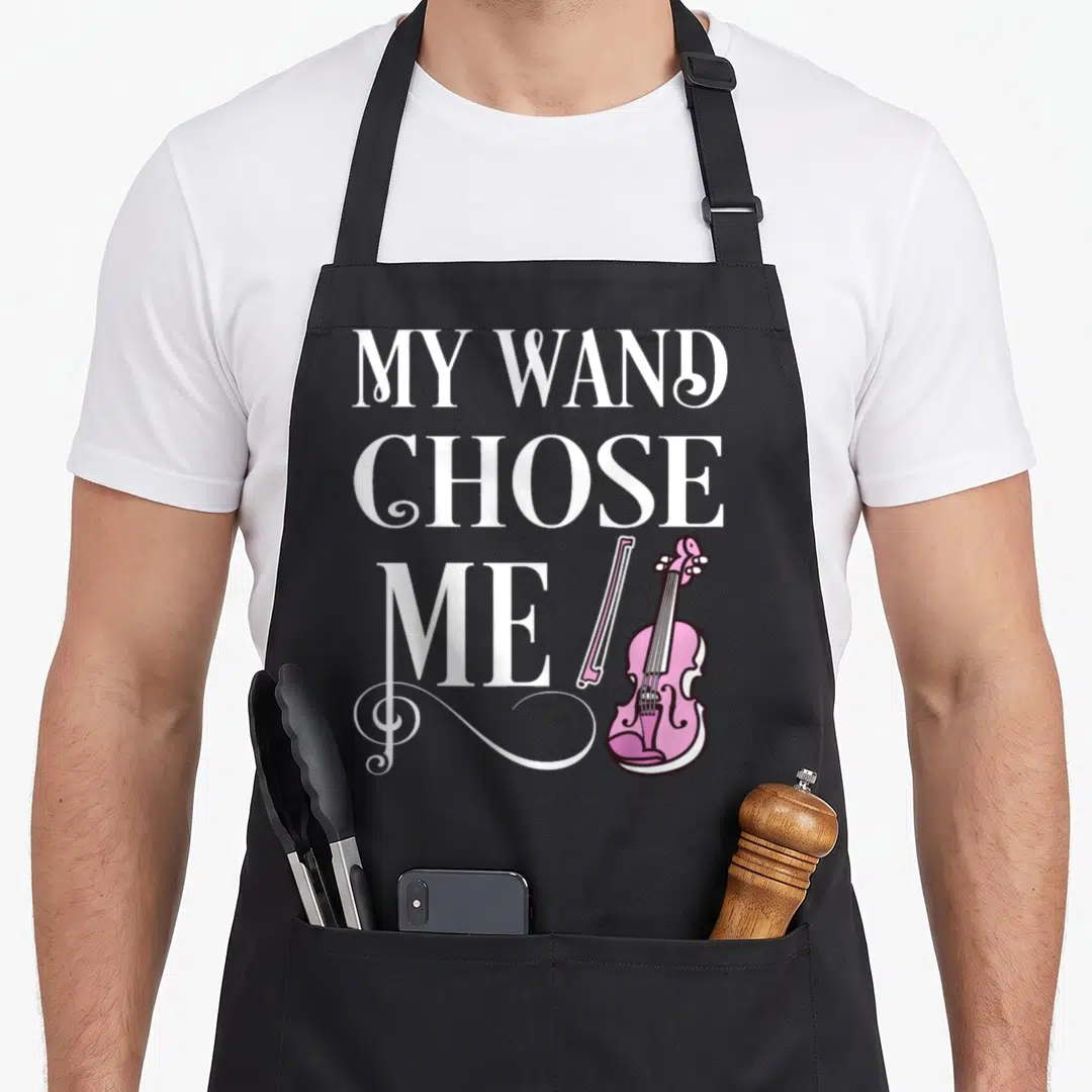 Wand violinist apron - White stacked text reading My Wand Chose Me beside pink violin and treble clef flourish — shown on a black cotton canvas apron against a white background