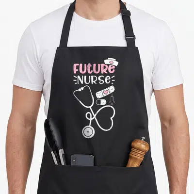 Vintage future nurse apron - Distressed pink and white FUTURE NURSE text above a stethoscope heart, bandage, pill — shown on a black cotton canvas apron against a white background