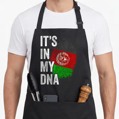 Afghanistan pride apron - IT'S IN MY DNA text beside a fingerprint filled with white, black, red, and green flag colors — shown on a black cotton canvas apron against a white background