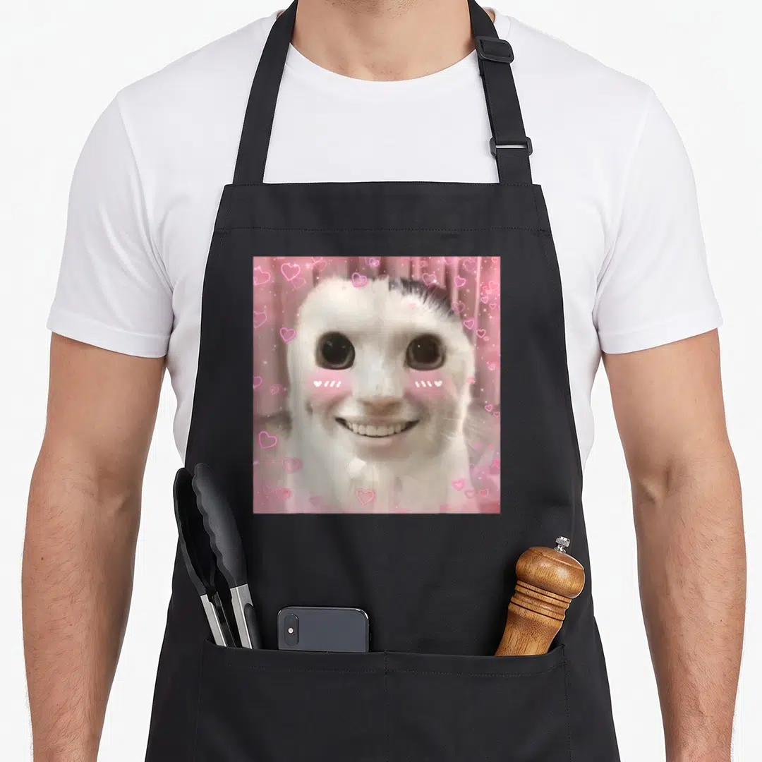 Ahh banana apron - White cat head centered among scattered pink hearts on a pink background — shown on a black cotton canvas apron against a white background