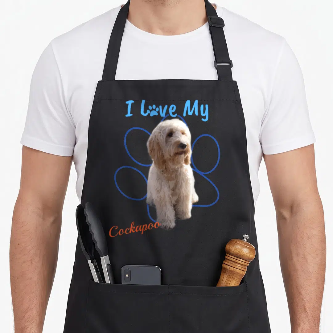 Paw cockapoo apron - I Love My Cockapoo text with photo-style dog and blue paw print outline — shown on a black cotton canvas apron against a white background