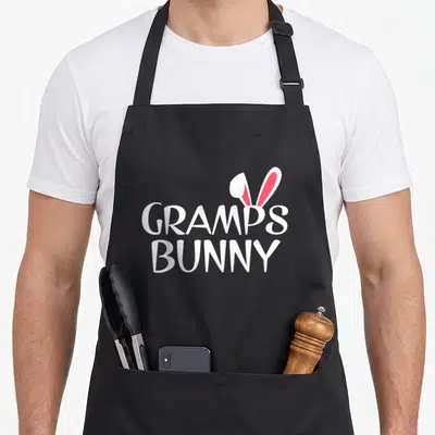 Gramp easter bunny aprons - Stacked white text GRAMPS BUNNY with two white and red bunny ears emerging from behind — shown on a black cotton canvas apron against a white background