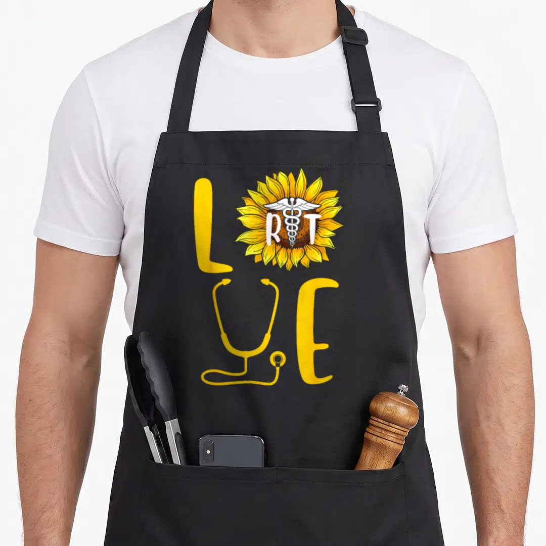 Sunflower nurse apron - LOVE text with sunflower containing RT and caduceus, yellow stethoscope replacing V — shown on a black cotton canvas apron against a white background
