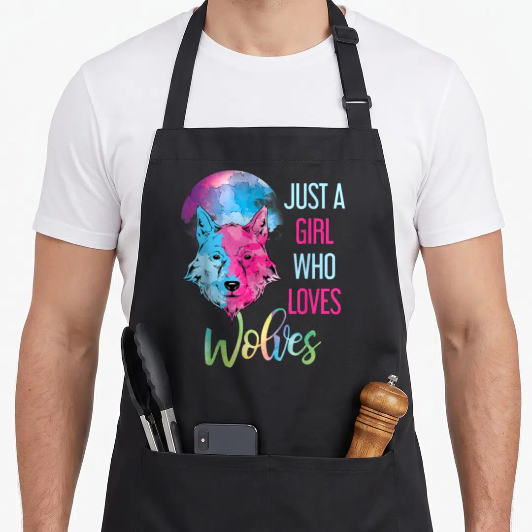 Moonlight predator apron - Cartoon wolf head in pink and blue with stacked text JUST A GIRL WHO LOVES Wolves — shown on a black cotton canvas apron against a white background