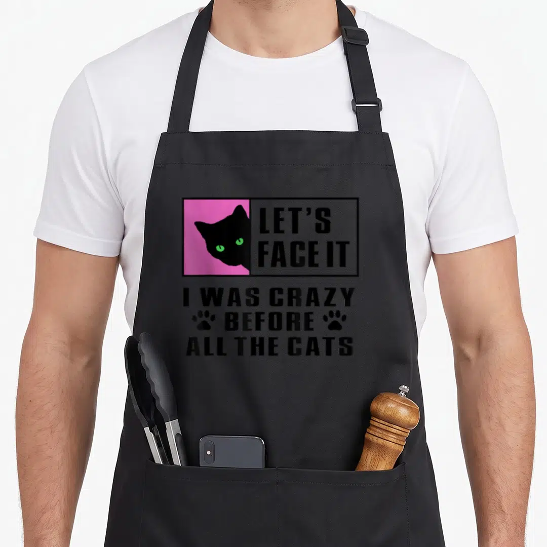 Before crazy cat lady apron - Black cat in pink square with sarcastic text about being crazy before all the cats — shown on a black cotton canvas apron against a white background