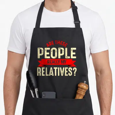 These family reunion aprons - Red ribbon banner with beige text reading Are These People Really My Relatives — shown on a black cotton canvas apron against a white background