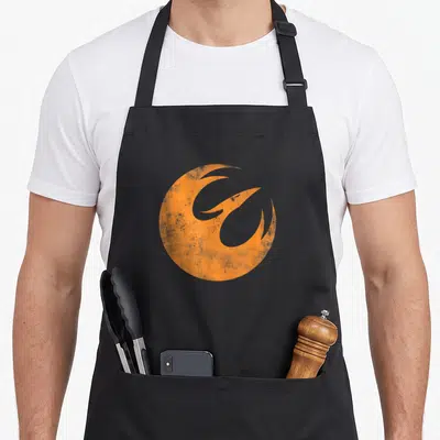 Rebel phoenix apron - Orange circular phoenix silhouette with distressed texture on grey background — shown on a black cotton canvas apron against a white background
