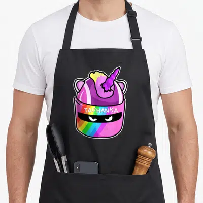 Komodo cartoon apron - Pink helmet with unicorn horn, rainbow stripes, and TACHANKA text — shown on a black cotton canvas apron against a white background