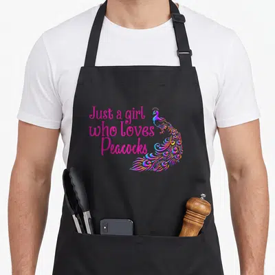 Animal apron for the kitchen - Pink text reading Just a girl who loves Peacocks next to a colorful peacock illustration — shown on a black cotton canvas apron against a white background