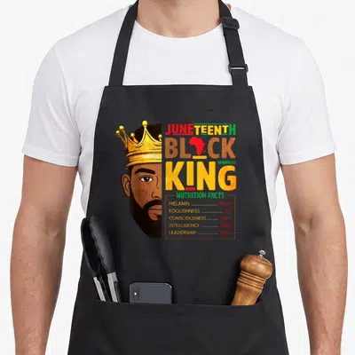 Juneteenth king apron - Crowned man half-face beside nutrition facts listing 100 percent melanin and intelligence — shown on a black cotton canvas apron against a white background