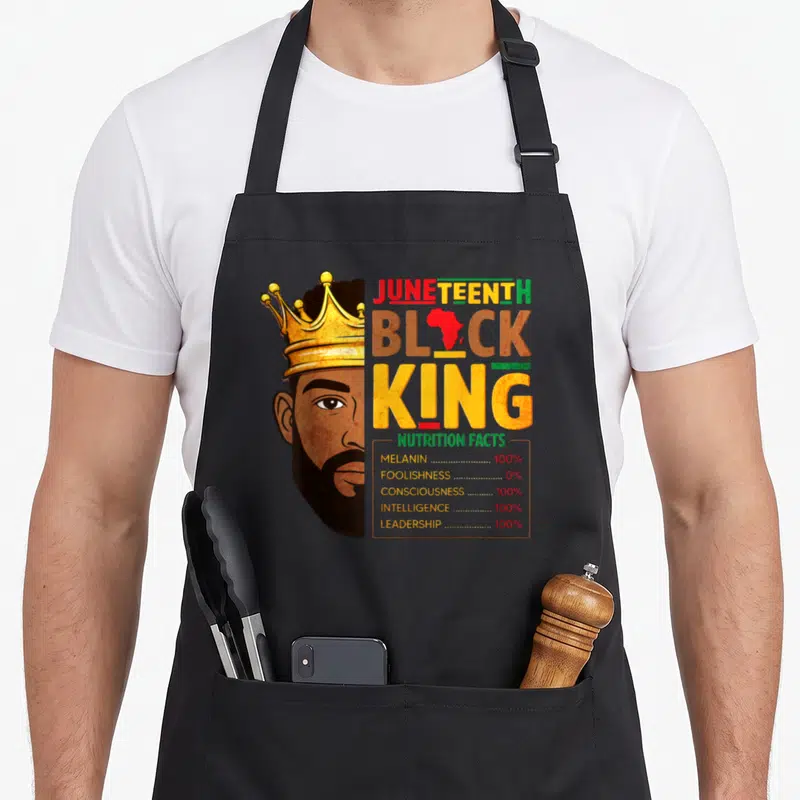 Juneteenth king apron - Crowned man half-face beside nutrition facts listing 100 percent melanin and intelligence — shown on a black cotton canvas apron against a white background