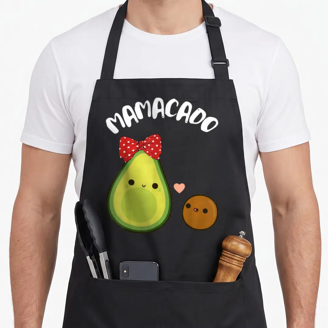 Mamacado avocado apron - Cartoon avocado with red bow and brown pit character under arched text — shown on a black cotton canvas apron against a white background