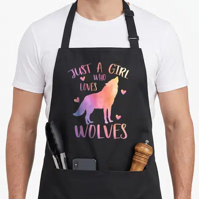 Funny watercolor wolves apron - Purple pink orange watercolor wolf howling with Just a Girl Who Loves Wolves text — shown on a black cotton canvas apron against a white background
