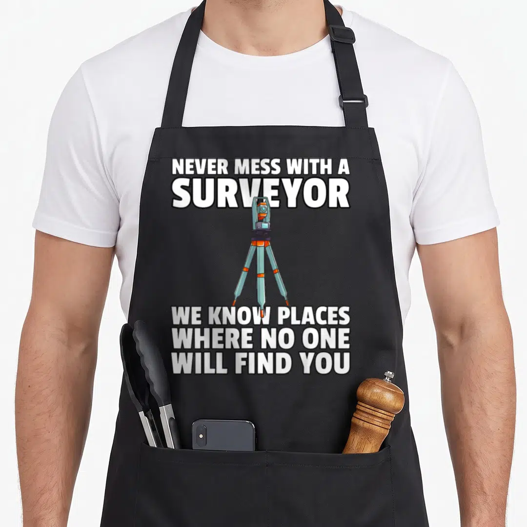 Land recorder apron - Cartoon theodolite on tripod with white text NEVER MESS WITH A SURVEYOR WE KNOW PLACES — shown on a black cotton canvas apron against a white background