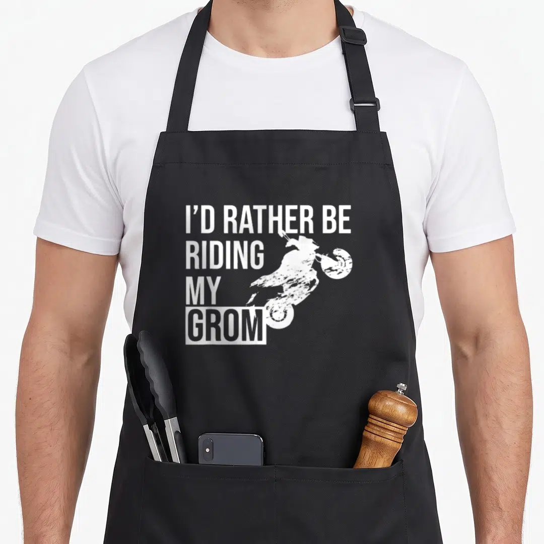 Rather i love riding apron - Stacked white text reading I'd Rather Be Riding My Grom beside a distressed wheelie — shown on a black cotton canvas apron against a white background