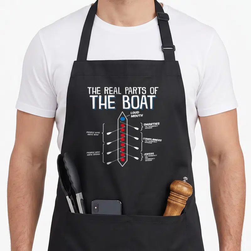 Boat parts of an apron - Cartoon boat diagram labeling rowers as loud mouth, smarties, complainers, and jokers in white — shown on a black cotton canvas apron against a white background