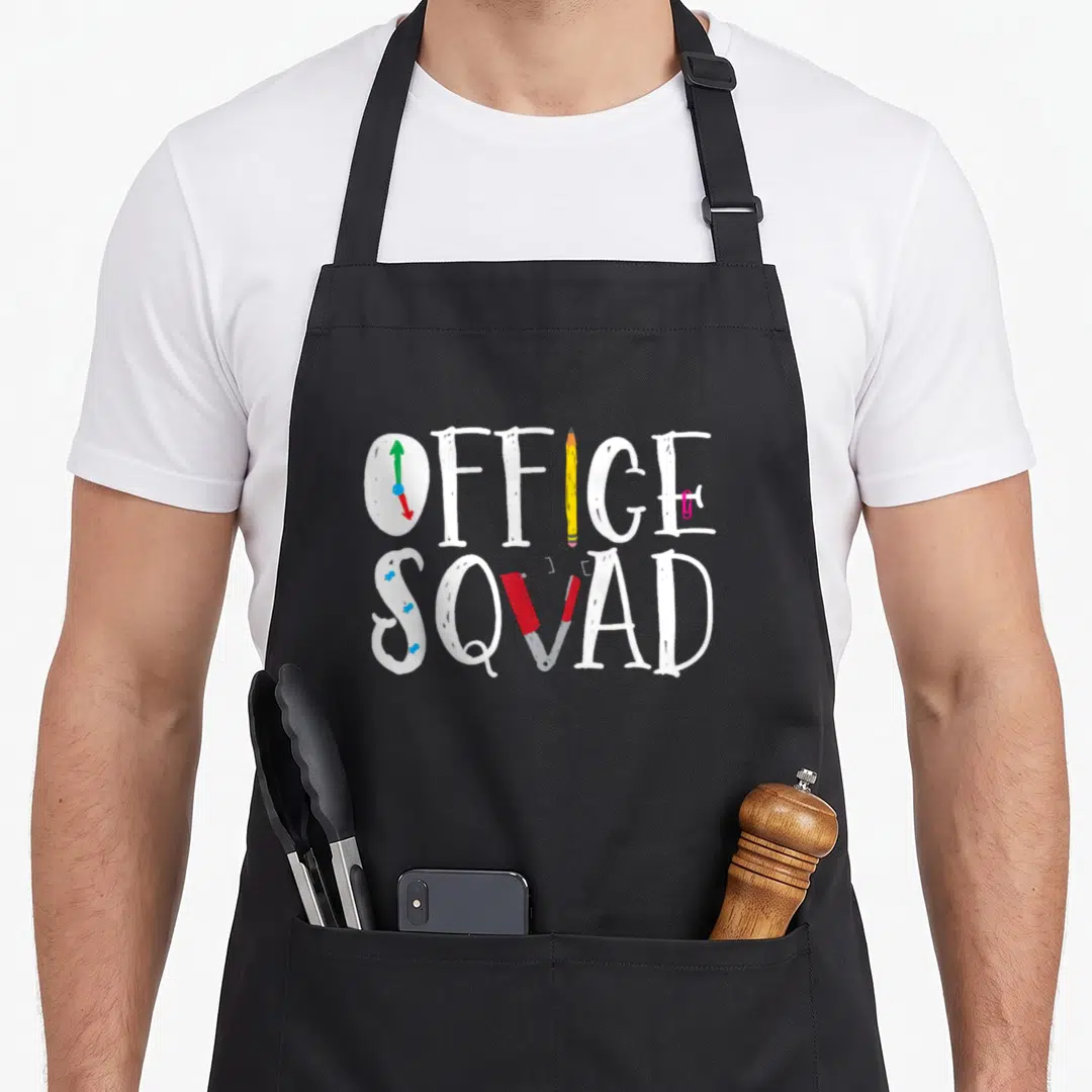 Assistant squad office apron - OFFICE SQVAD text with clock pencil stapler and pushpins in white yellow red blue pink — shown on a black cotton canvas apron against a white background