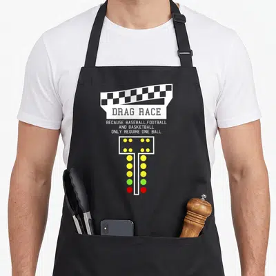 Drag christmas apron - Checkered flag, drag race text, and vertical light tree with yellow green and red lights — shown on a black cotton canvas apron against a white background
