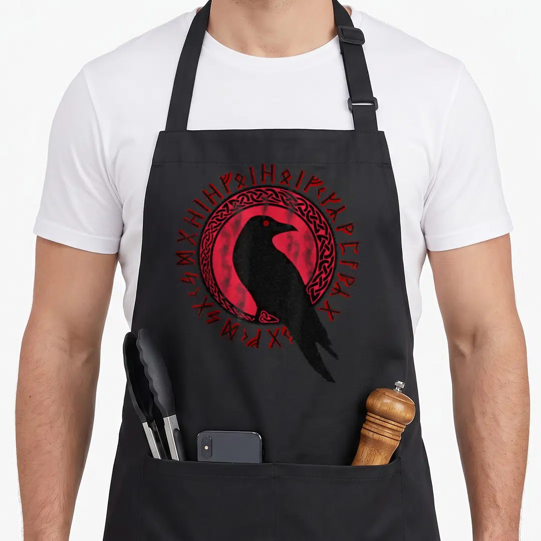 Odin viking apron - Black raven inside red circle with knotwork ring and surrounding red runes on distressed print — shown on a black cotton canvas apron against a white background