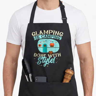 Glamping camper camping apron - Retro light blue camper trailer with bunting flags and slogan Glamping Is Camping Done — shown on a black cotton canvas apron against a white background