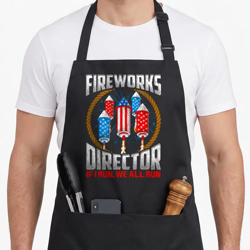 Director 4th of july apron - Distressed fireworks director graphic with four patriotic rockets and safety warning text — shown on a black cotton canvas apron against a white background