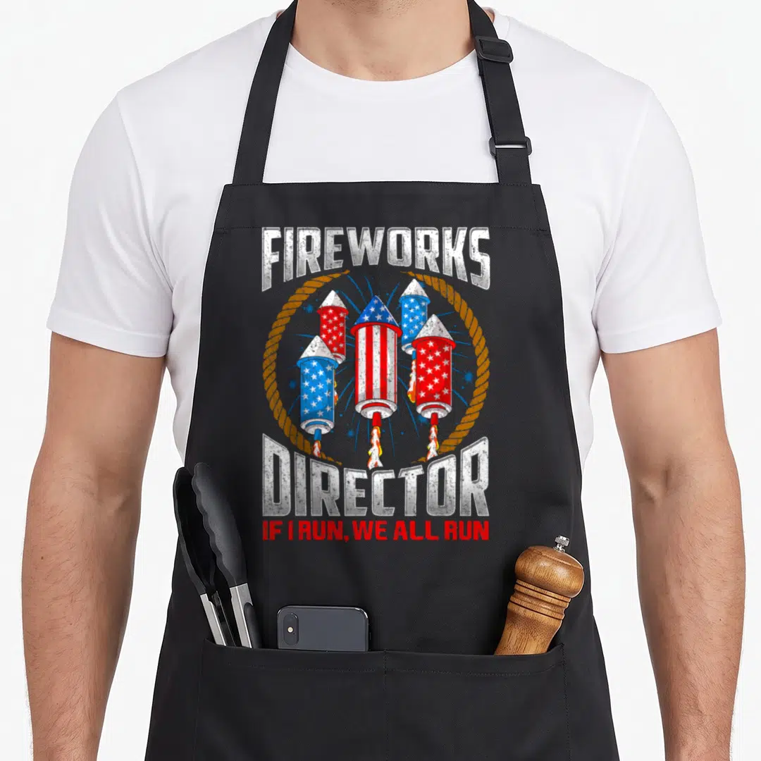 Director 4th of july apron - Distressed fireworks director graphic with four patriotic rockets and safety warning text — shown on a black cotton canvas apron against a white background