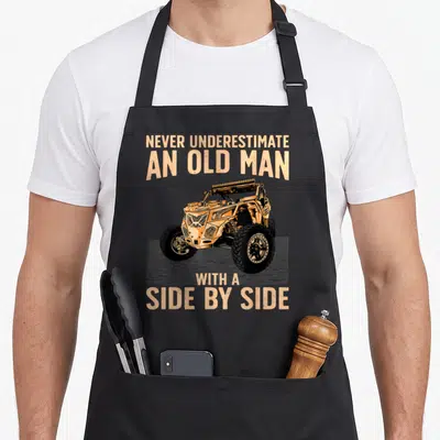 Sxs grandpa apron - Orange UTV with text Never Underestimate An Old Man With A Side By Side on grey background — shown on a black cotton canvas apron against a white background