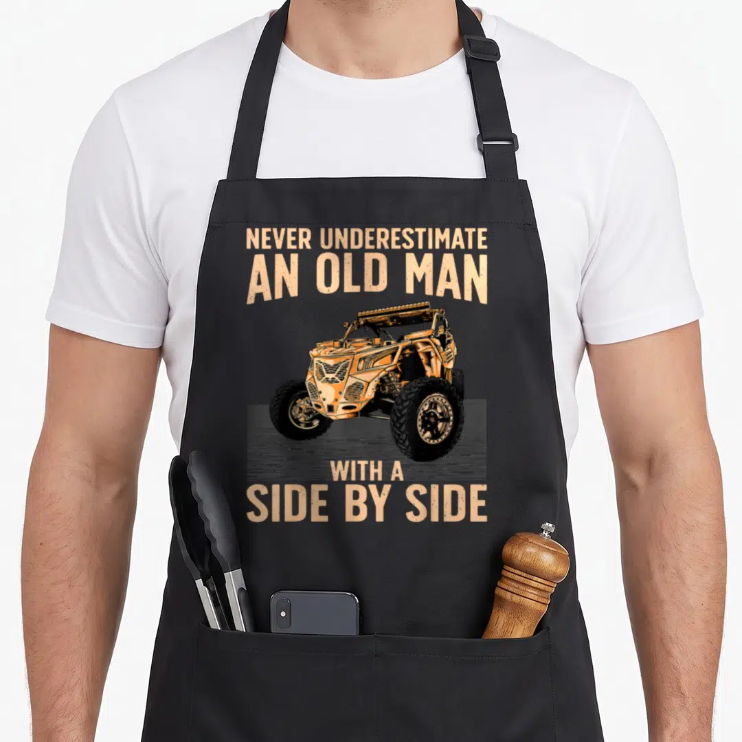 Sxs grandpa apron - Orange UTV with text Never Underestimate An Old Man With A Side By Side on grey background — shown on a black cotton canvas apron against a white background