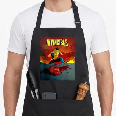 Omni bloody apron - INVINCIBLE text above superhero standing over bloody reflection in burning city — shown on a black cotton canvas apron against a white background