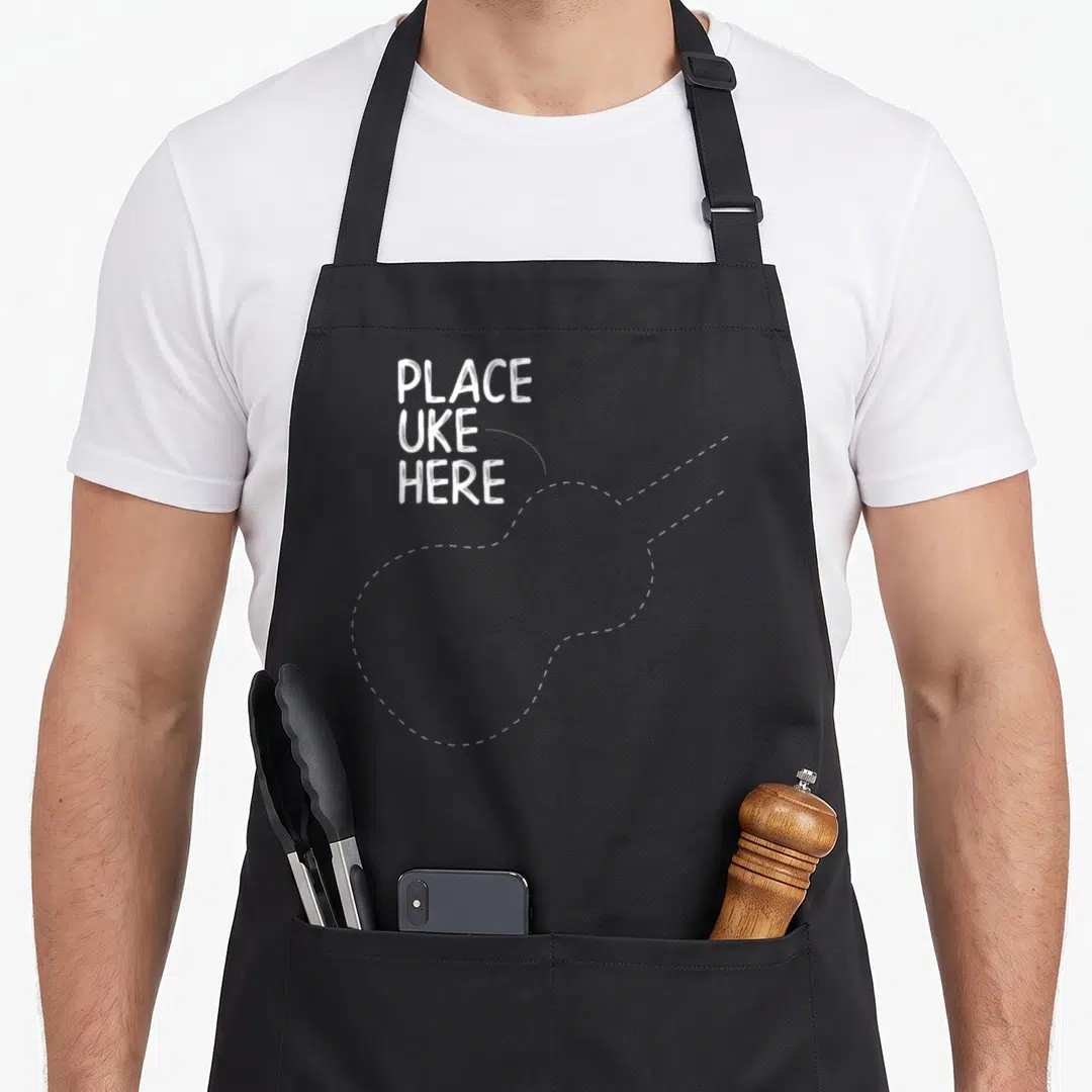 Accessory ukulele apron - White stacked text reading PLACE UKE HERE next to a dashed ukulele outline — shown on a black cotton canvas apron against a white background