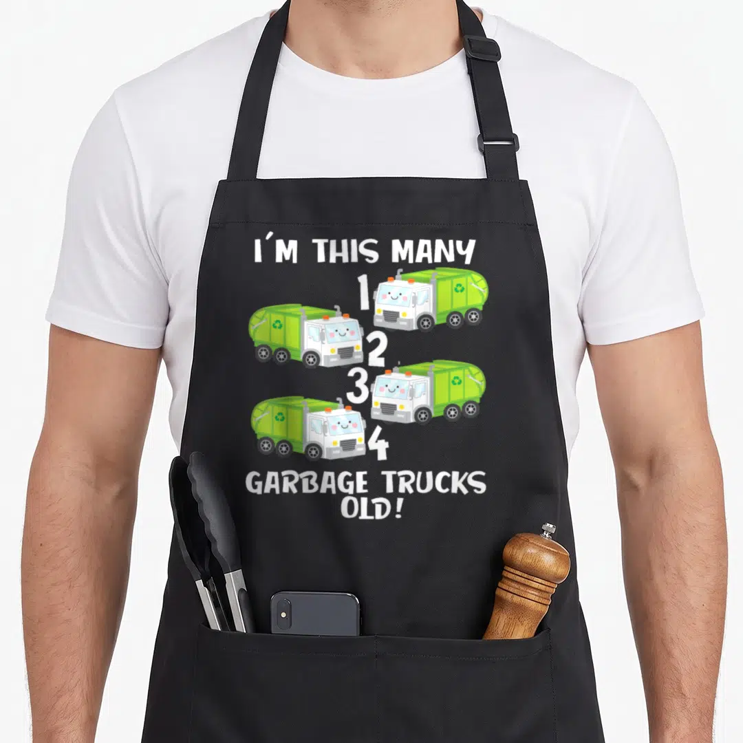 Counting truck apron - Four green cartoon garbage trucks numbered one to four with text I'M THIS MANY GARBAGE TRUCKS — shown on a black cotton canvas apron against a white background