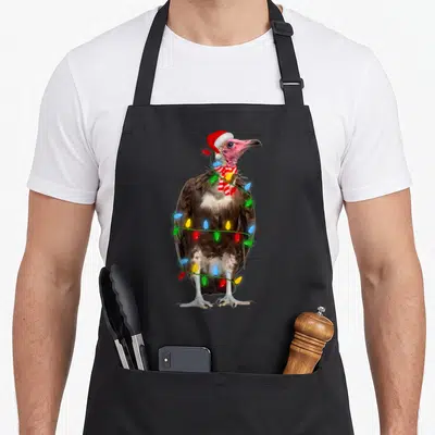 Vulture holiday christmas aprons - Standing vulture in Santa hat striped scarf wrapped in colorful Christmas lights — shown on a black cotton canvas apron against a white background