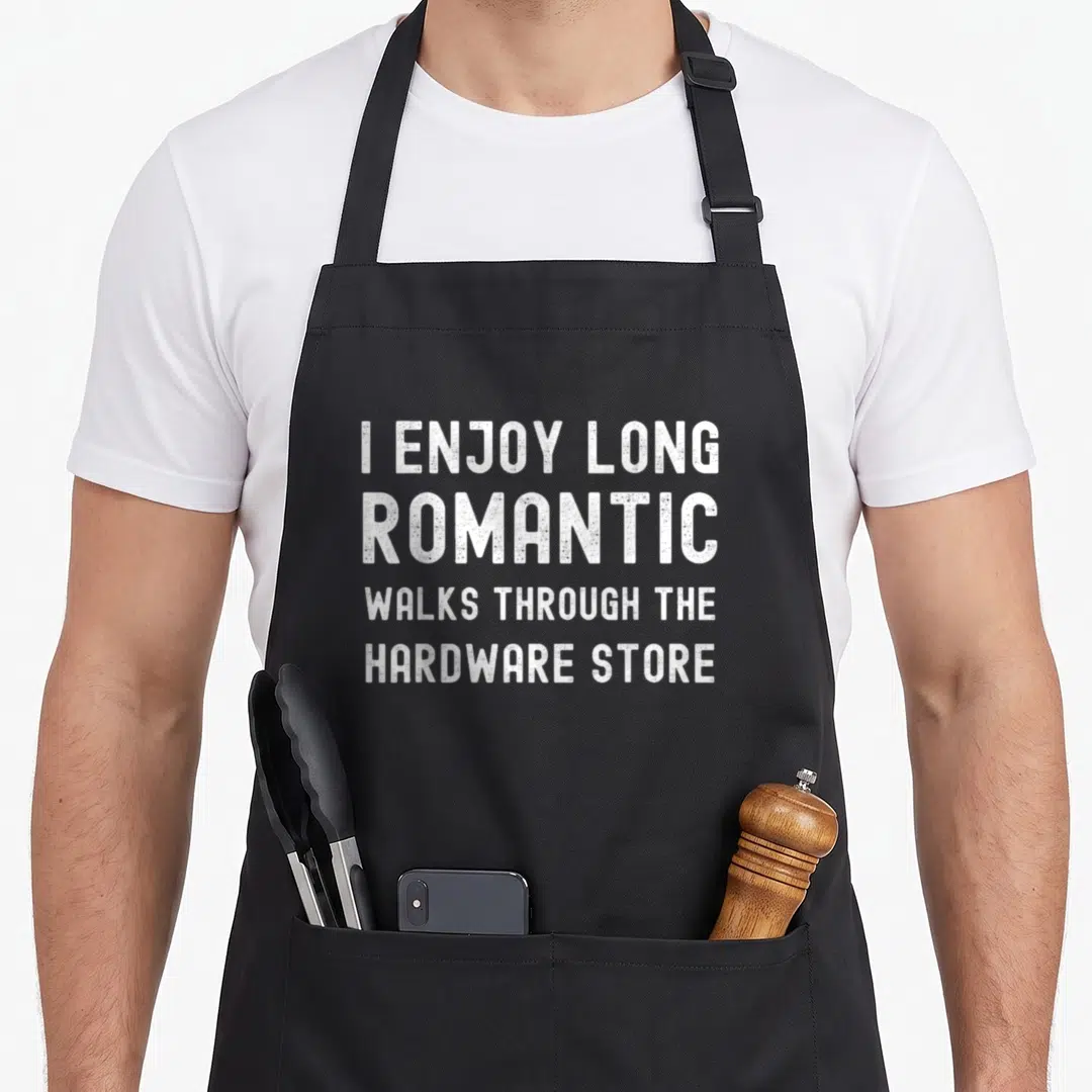Father handyman apron - White stacked text reading I Enjoy Long Romantic Walks Through the Hardware Store — shown on a black cotton canvas apron against a white background